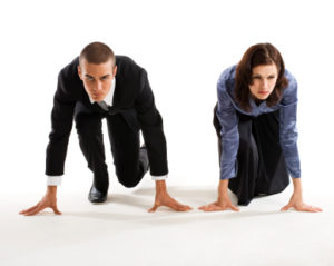 Young businesswoman and young businessman side-by-side in starting position and determined to win. Concepts: competition; corporate race; power struggle; battle of the sexes. Studio photography, isolated on white background.